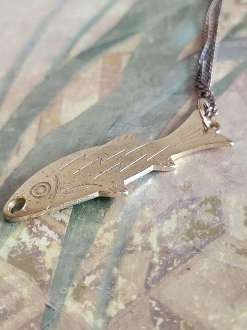 May include: A silver fish pendant necklace with a detailed design. The pendant is attached to a silver chain.