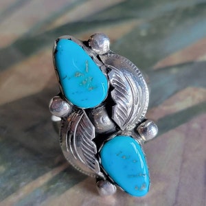 May include: A silver ring with two turquoise stones set in a leaf design.