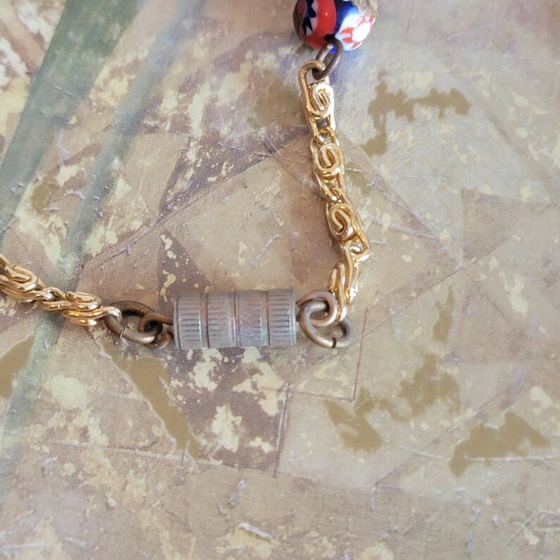 May include: A gold chain necklace with a silver clasp and a colorful glass bead. The bead has red, white, and blue colors.