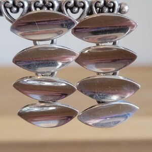May include: A pair of silver earrings with a chain-like design. Each earring has four oval-shaped links.