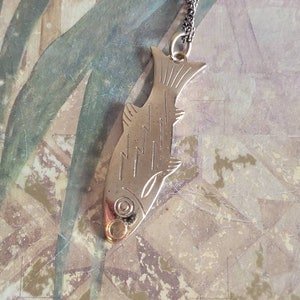 May include: A silver fish pendant necklace with a detailed design. The pendant is attached to a silver chain.