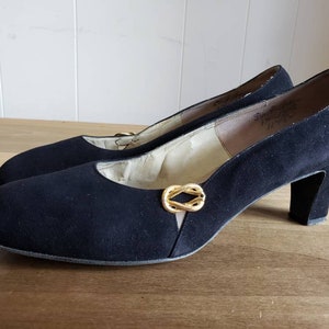 May include: Black suede pumps with a gold buckle detail and a low block heel.