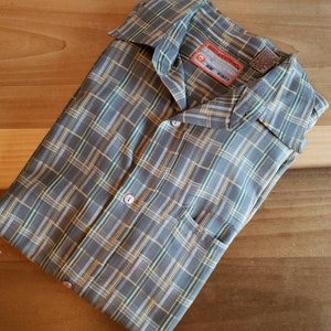 May include: A gray, yellow, and green plaid button-down shirt with a pocket on the left side. The shirt has a label that reads "Rock & Republic" and "Size L (32-33)".