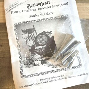 May include: A white instruction booklet titled "Braid Craft Fabric Braiding Basics for Everyone!" by Shirley Botsford. The booklet features a black and white illustration of a braided chair and accessories. Silver braiding tools are visible.