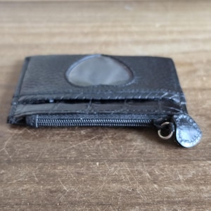 May include: A black card holder with a textured surface, featuring a heart-shaped cutout window on the front and a zippered compartment. The zipper pull is shaped like a small heart, and the front pocket has a glossy, embossed crocodile-like pattern.