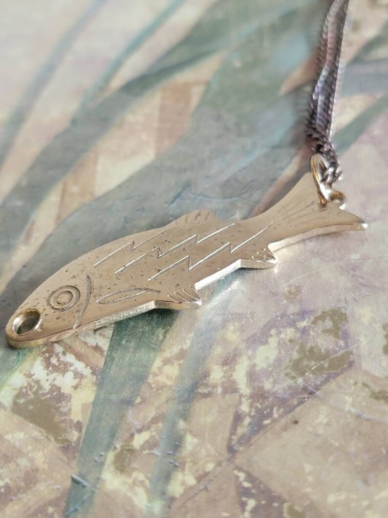May include: A silver fish pendant necklace with a detailed design. The pendant is attached to a silver chain.