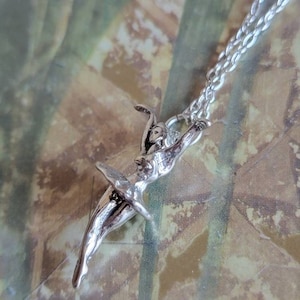 May include: A silver necklace with a ballerina charm. The ballerina is in a mid-air pose with her arms outstretched.