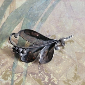 May include: A silver leaf-shaped brooch with a cluster of small round beads. The brooch is made of oxidized silver and has a vintage style.