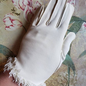 May include: A pair of white gloves with a fringed edge. The gloves are made of a soft, smooth fabric.