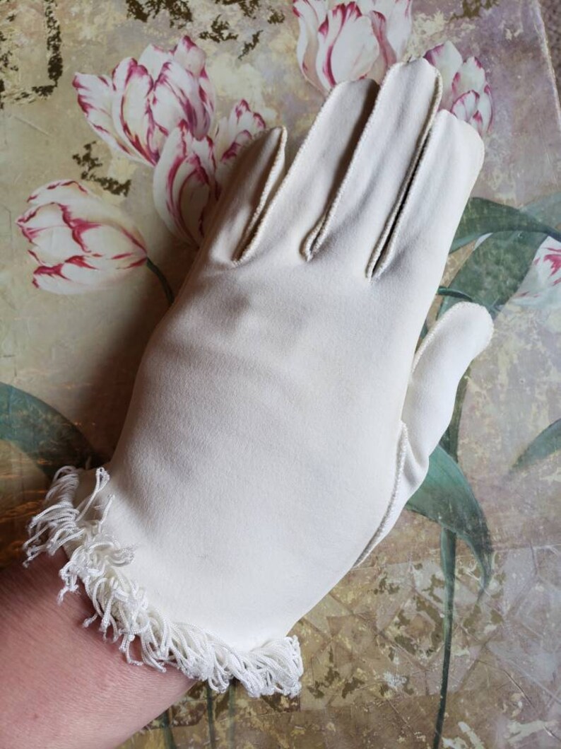 May include: A pair of white gloves with a fringed edge. The gloves are made of a soft, smooth fabric.
