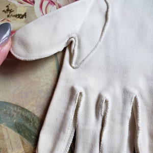May include: A pair of white cotton gloves with a delicate white stitching detail around the edges.