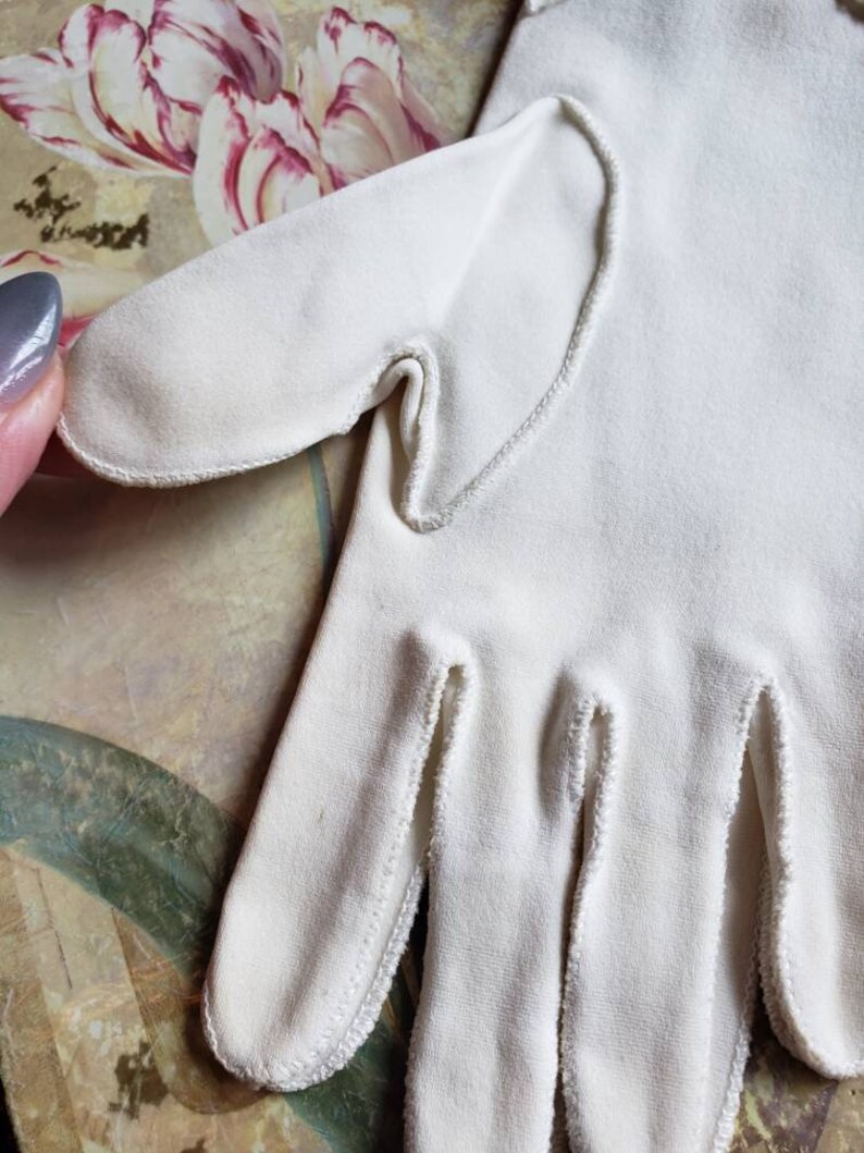May include: A pair of white cotton gloves with a delicate white stitching detail around the edges.