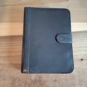 May include: A black leather binder with a flap closure and a single button.