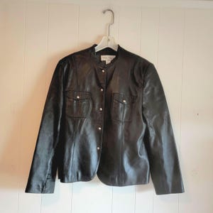 May include: A black leather jacket with a snap button closure, two flap pockets, and a mandarin collar.
