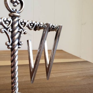 May include: A pair of silver triangle shaped earrings hanging on a decorative stand.