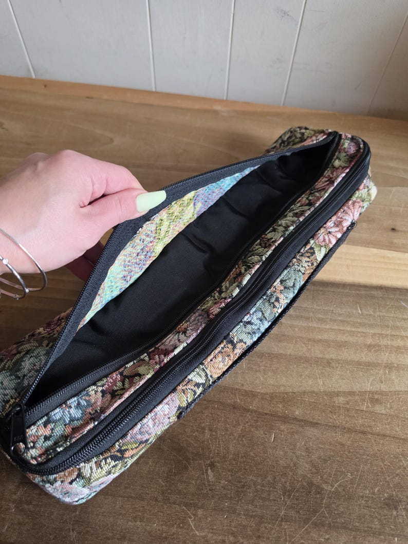 Puede incluir: Estuche de l&aacute;pices abierto de tapiz floral con cremallera negra. El interior es negro. El estuche est&aacute; abierto, revelando el forro interior. El estampado floral incluye colores rosa, verde y beige.