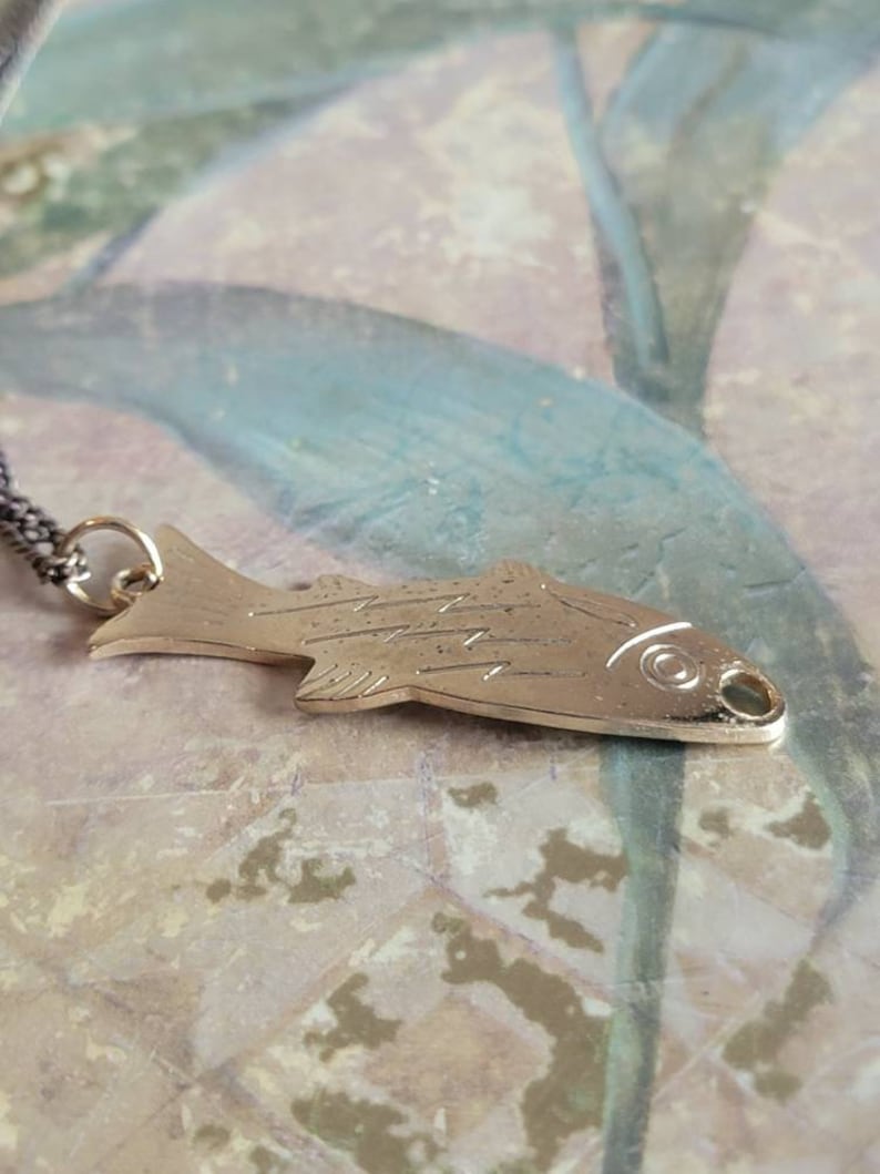 May include: A silver fish pendant necklace with a detailed design. The pendant is hanging on a silver chain.