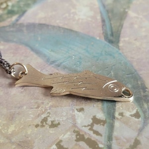 May include: A silver fish pendant necklace with a detailed design. The pendant is hanging on a silver chain.