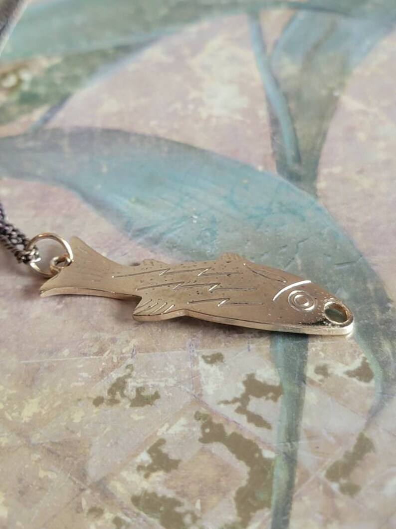 May include: A silver fish pendant necklace with a detailed design. The pendant is hanging on a silver chain.
