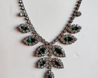 May include: A silver necklace with a delicate chain and a pendant featuring a cluster of green and clear rhinestones in a leaf design.