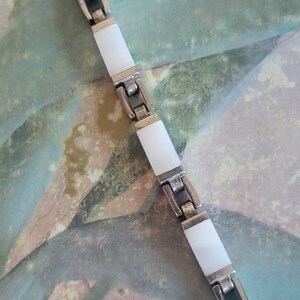 May include: A silver bracelet with white rectangular links. The bracelet is made of metal and has a polished finish.