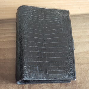 Puede incluir: Un diario encuadernado en cuero negro con un patr&oacute;n de cocodrilo en relieve.