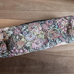 Puede incluir: Un estuche rectangular con un dise&ntilde;o de tapiz floral. El estuche tiene un cierre de cremallera y est&aacute; cubierto con un patr&oacute;n de flores y follaje rosas, verdes y marrones. El estuche mide aproximadamente 23 cm de largo.