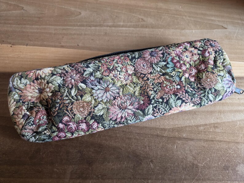 Puede incluir: Un estuche rectangular con un dise&ntilde;o de tapiz floral. El estuche tiene un cierre de cremallera y est&aacute; cubierto con un patr&oacute;n de flores y follaje rosas, verdes y marrones. El estuche mide aproximadamente 23 cm de largo.
