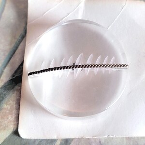 May include: A clear glass button with a brown and gold braided wire design across the center.