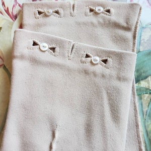 May include: A pair of beige tights with delicate white bows and buttons at the top. The bows are stitched with a decorative stitch.