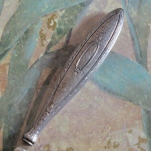 May include: Silver-plated handle with an ornate design and a hammered finish. The handle has a raised oval with an inscription inside.