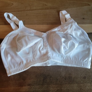 May include: A white bra with adjustable straps and a full-coverage design. The bra features a satin-like fabric with delicate lace detailing along the edges and center. The cups are softly molded, offering support and a smooth silhouette.