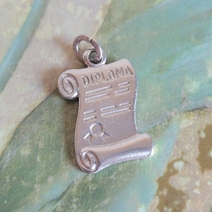 May include: Silver charm in the shape of a rolled up diploma with the word "DIPLOMA" printed on it.