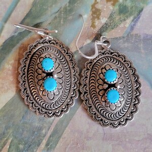 May include: A pair of silver earrings with turquoise stones. The earrings are oval shaped and have a detailed design.