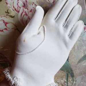 May include: A pair of white gloves with a frilled edge. The gloves are made of a soft, smooth fabric.