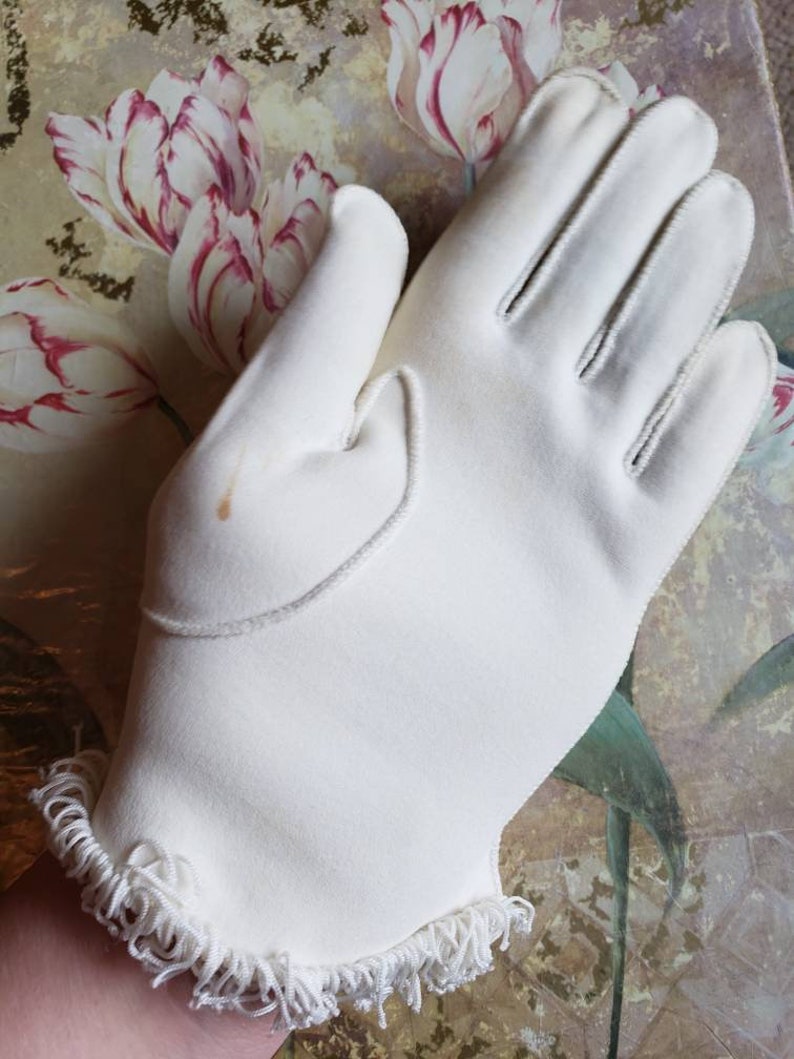 May include: A pair of white gloves with a frilled edge. The gloves are made of a soft, smooth fabric.