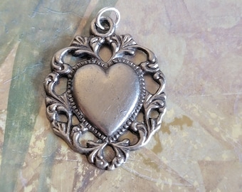 May include: A silver heart-shaped pendant with an ornate filigree design. The pendant has a loop at the top for attaching to a chain.