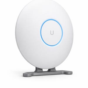Pode incluir: Um ponto de acesso sem fio branco e circular com um anel iluminado azul e uma base cinza. O dispositivo tem um design simples e moderno, com a letra "U" no centro do anel.
