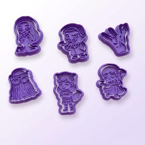 Pode incluir: Seis cortadores de biscoitos de plástico roxo em várias formas com tema de Halloween. As formas incluem um fantasma, um zumbi, uma mão, uma figura com óculos, uma menina com um gato e uma menina com um vestido.