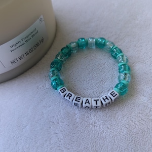 May include: A turquoise and white beaded bracelet with the word "BREATHE" spelled out in white letter beads.