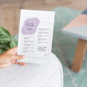 May include: A white card with the word "Faith-ism" in a handwritten font, with a purple blob design. The card contains a list of text and the phrase "I don't need certainty - I need God." The card is held by a person.