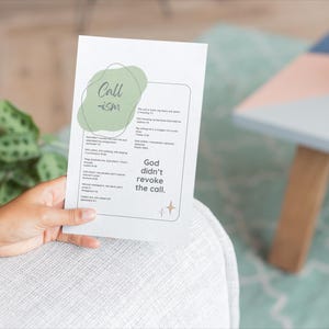 May include: A white card with the text "Call ISM" in green and a list of text. The card is held by a person. The background includes a plant in a pot and a small table with a geometric design.