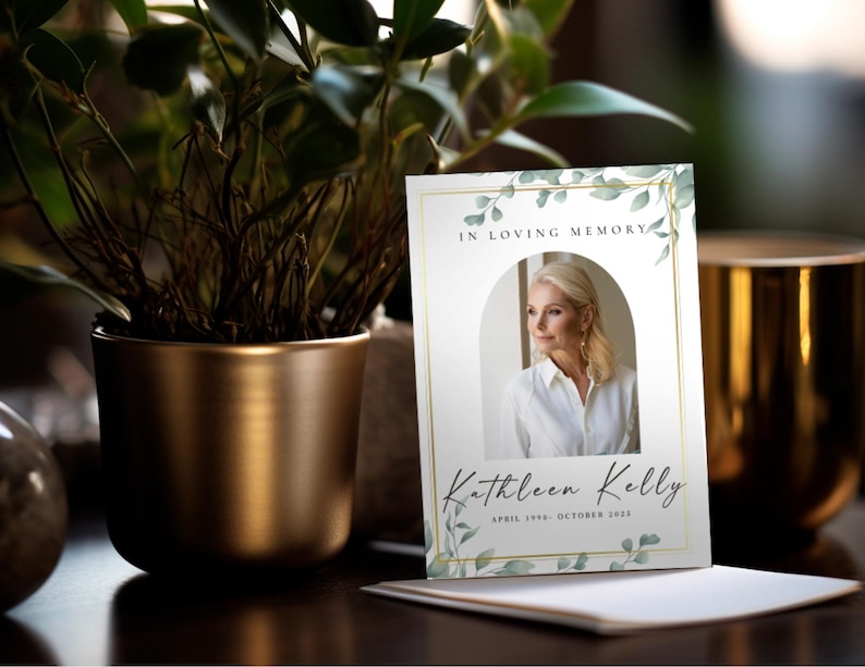 Op de afbeelding: Een herdenkingskaart met de tekst "In Loving Memory" en de naam "Kathleen Kelly". De kaart toont een foto van een vrouw en is versierd met groene bladeren en een gouden rand. Een potplant en een gouden kandelaar staan op de achtergrond.