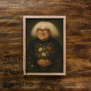 Peut inclure: Un portrait encadré d'une personne souriante aux cheveux blancs et aux lunettes, tenant un bouquet de fleurs. La personne porte un pull noir orné de détails floraux. Les mots "Just Danny DeVito" sont imprimés sur le fond en bois.