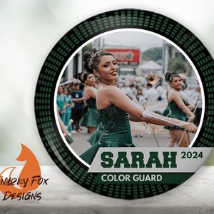 May include: A green and black circular button with a photo of a young woman in a green dress holding a baton. The text "SARAH 2024 COLOR GUARD" is printed on the button.
