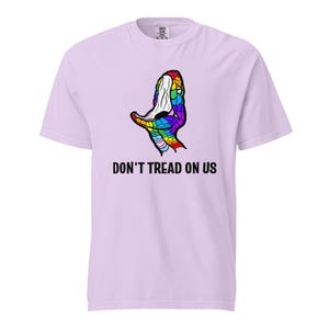 Op de afbeelding: Lichtpaarse t-shirt met een kleurrijke slangenkop afbeelding. De slangenkop is ontworpen met regenboogkleuren. Onder de afbeelding staat de tekst "DON'T TREAD ON US".