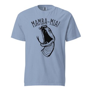 Puede incluir: Camiseta azul claro con un gráfico negro de la cabeza de una serpiente con la boca abierta. El texto "MAMBA-MIA!" está arqueado sobre la cabeza de la serpiente en una fuente lúdica. La camiseta es de un material suave.