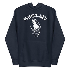 Puede incluir: Sudadera con capucha azul marino con un gráfico blanco de una cabeza de serpiente y el texto "MAMBA-MIA!". La sudadera tiene una capucha con cordón y un bolsillo delantero. El diseño está centrado en la parte delantera.