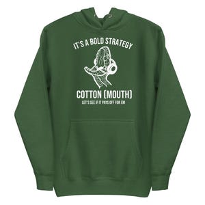 Puede incluir: Sudadera con capucha verde con bolsillo delantero y texto gráfico blanco. El texto dice "IT'S A BOLD STRATEGY" encima de una ilustración de boca de algodón, con "COTTON (MOUTH)" debajo y "LET'S SEE IF IT PAYS OFF FOR EM" en la parte inferior.