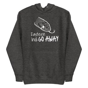 Peut inclure: Sweat à capuche gris foncé avec un motif blanc représentant une tête de serpent et le texte "Eastern Indi-GO AWAY". Le sweat à capuche est doté d'une capuche et d'une poche avant. Le motif est centré sur le devant.